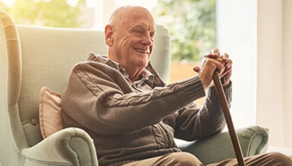 A smiling older gentleman with a cane sitting in a chair.