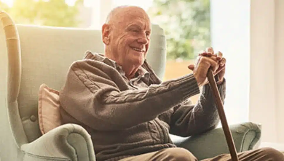 A smiling older gentleman with a cane sitting in a chair.
