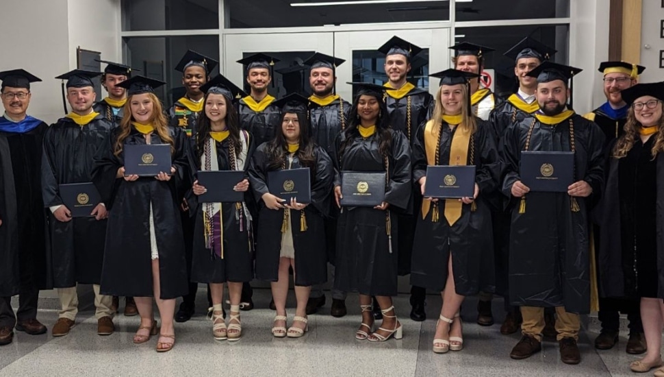 a group of students in cap and gown at wcu holding diplomas.