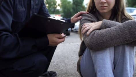 A police officer tries to comfort a young woman in distress sitting on the ground.