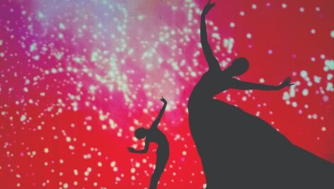 Silhouettes dancing against red backdrop.