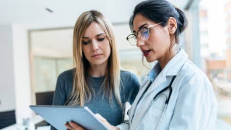 Female doctor talking while explaining medical treatment with digital tablet to patient in the consultation.