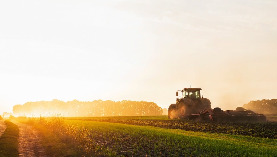 A farmer drives farm equipment out in a field.