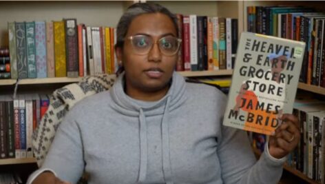 A woman holds up the book Heaven & Earth Grocery Store by James McBride.