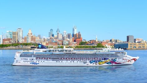 The Norwegian cruise liner Jewel sails on the water with the Philadelphia skyline in the background.