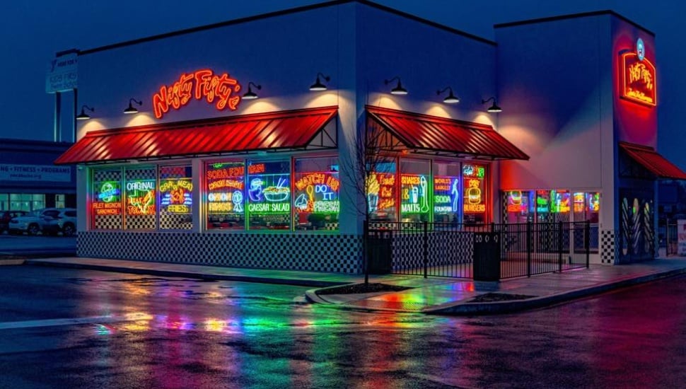 The neon-lit colorful exterior of a Nifty Fifty's restaurant at night.