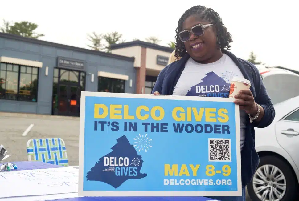 An enthusiastic volunteer holds a Delco Gives sign promoting the charitable giving day.