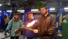 A trainer demonstrates a welding technique in front of two students.