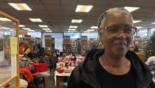 Denise Stinson, president of the Friends of the Yeadon Public Library, stands in the library with vendors from the Black Saturday Extravaganza in the background.