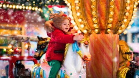 A little girl rides a carousel horse.