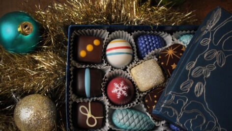 An open box of chocolate confections amidst tinsel and Christmas ball.