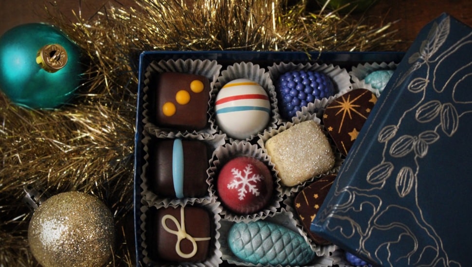 An open box of chocolate confections amidst tinsel and Christmas ball.