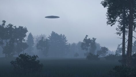 A UFO hovers in the sky over some woods.