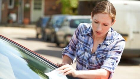 A distressed woman takes a parking ticket off of her windshield.