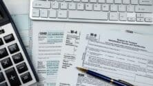 Different tax forms, including W-4s, 1099s and W-9s, laying on a table next to a calculator.