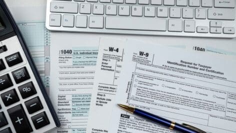 Different tax forms, including W-4s, 1099s and W-9s, laying on a table next to a calculator.