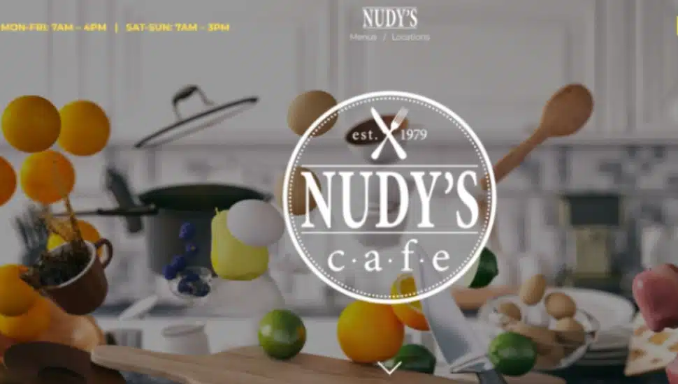 The home page of the Nudy's Cafe website showing fruit, spoons and kitchenware tossed about.