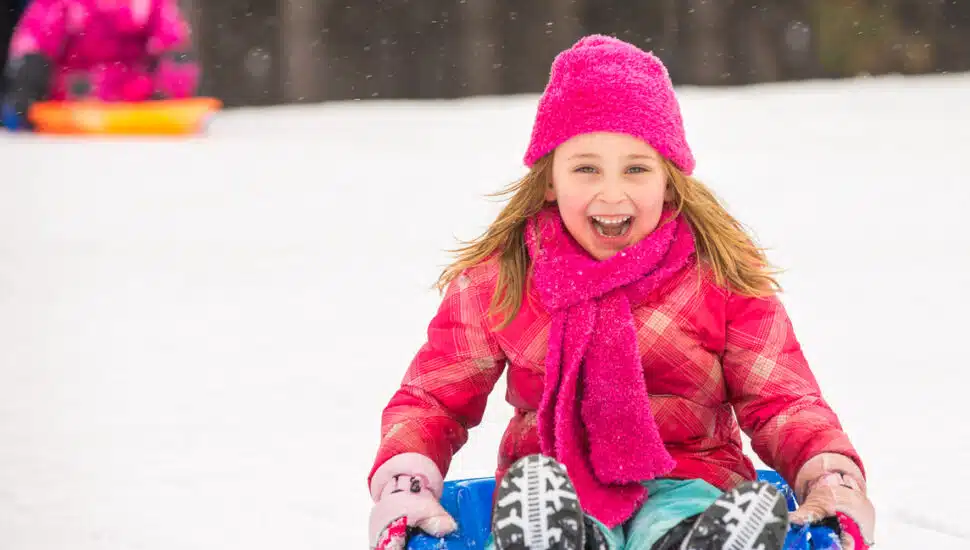 A happy girl dressed in pink sleds down a hill.
