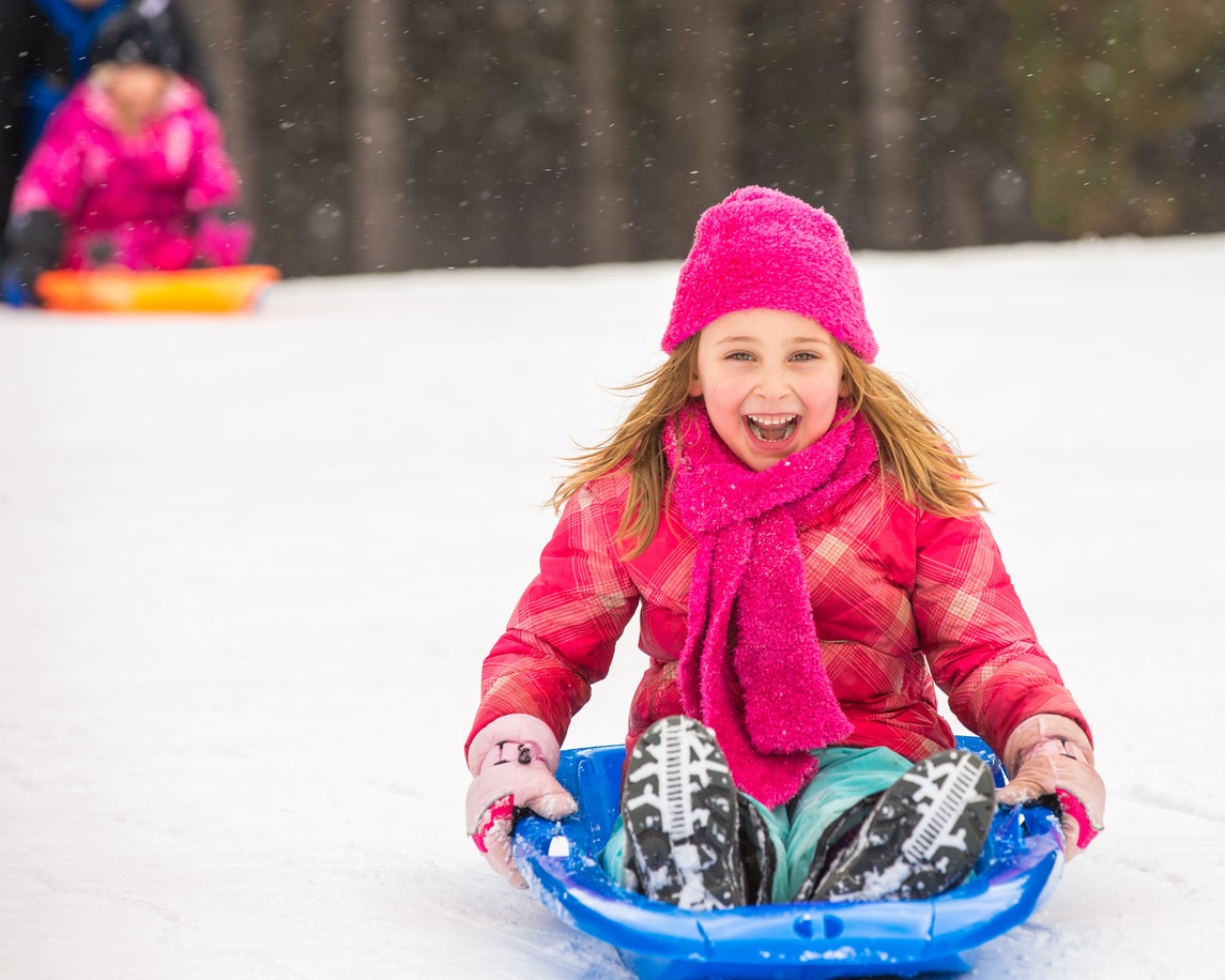 A happy girl dressed in pink sleds down a hill.