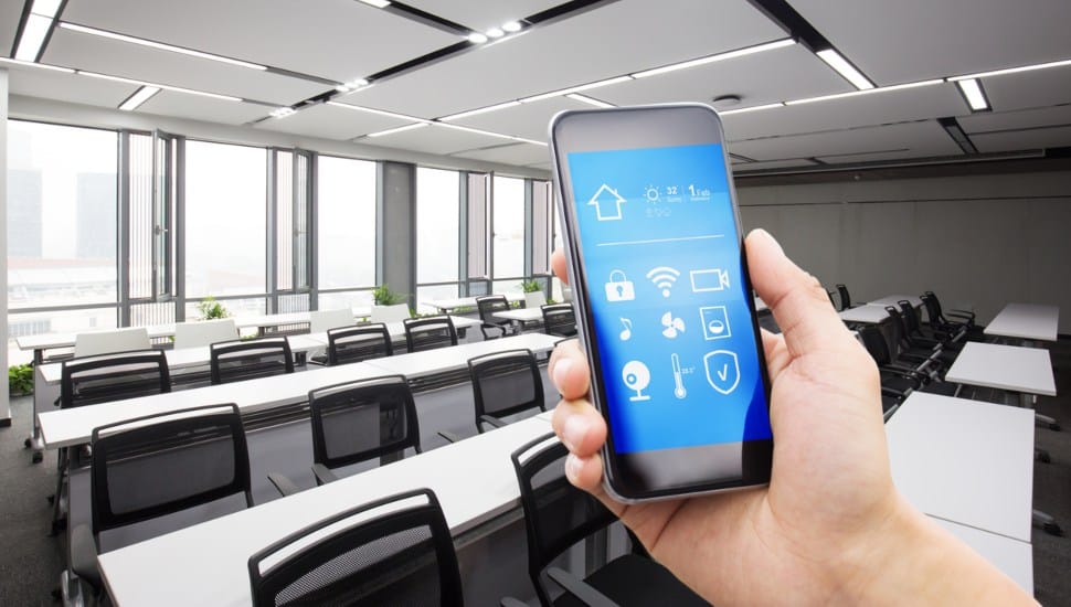 A hand holds up an iPhone in a classroom displaying apps.