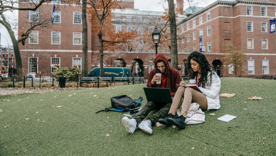 College students work while seated on the grass in the quad.