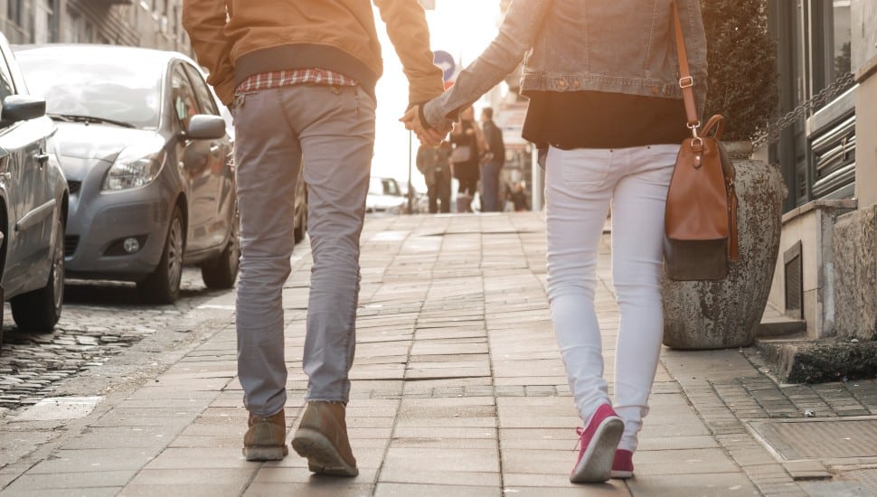 A couple holds hands as they walk along a sidewalk.