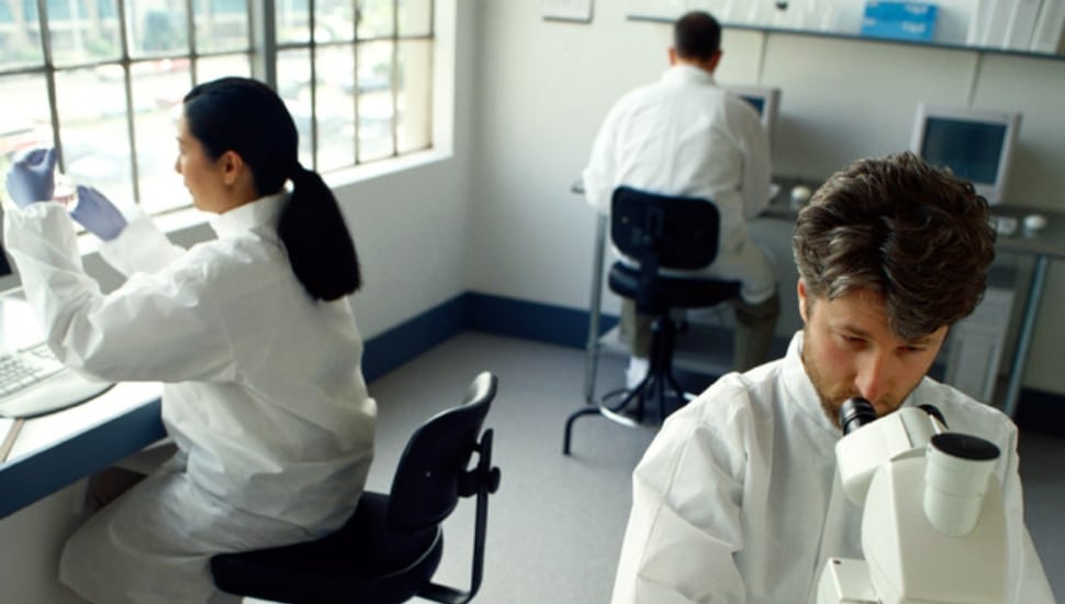 Researchers in white coats sitting at research stations.
