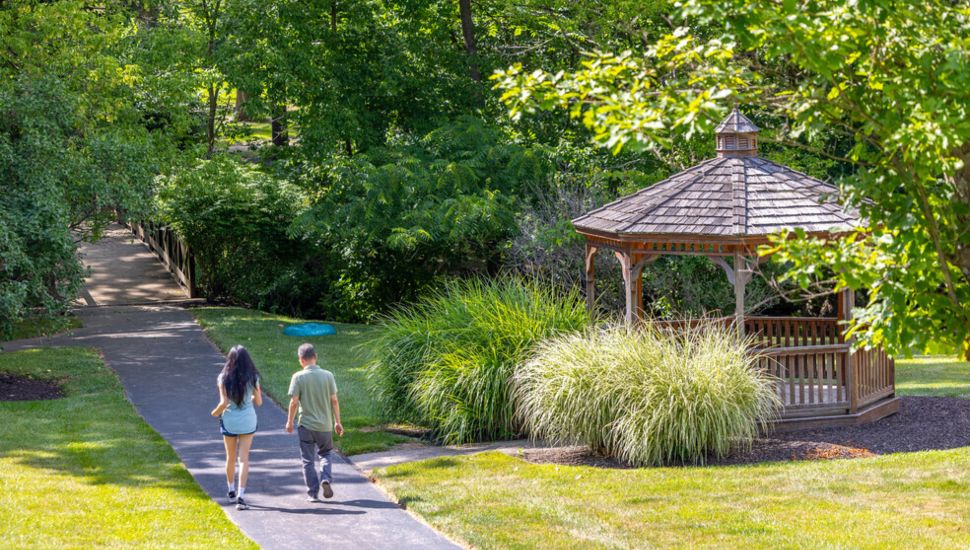 A couple walk a sunny path past a gazebo.