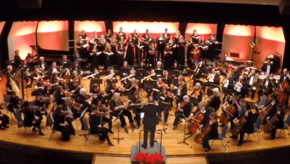 The Immaculata Symphony from above; the symphony is on stage playing in an auditorium, with composer in front.