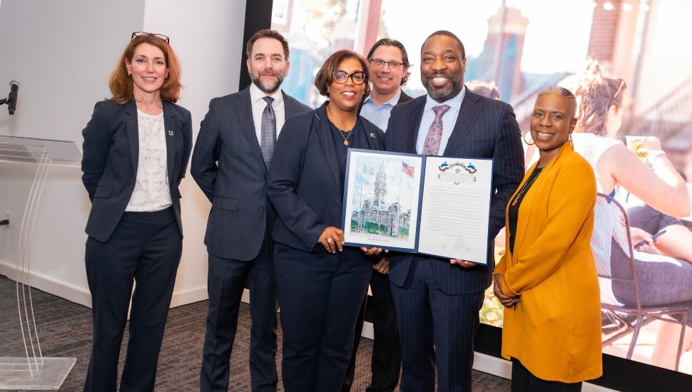 A group of men and women stand together holding a Philadelphia City Council resolution recognizing the 25-year anniversary of the Navy Yard.