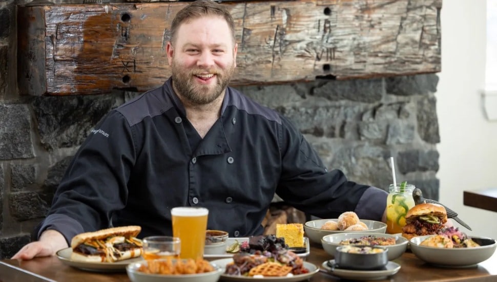 Executive chef and owner of Sophie's BBQ Greg Herman at a table with several food entrees.