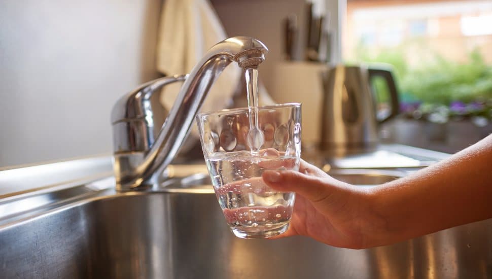 Close up of children hands, pouring glass of fresh water from tap in kitchen.