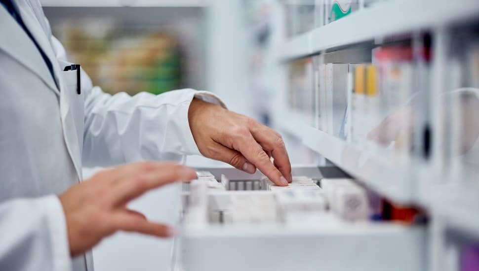 Someone in a lab coat is looking through bottles of pills.