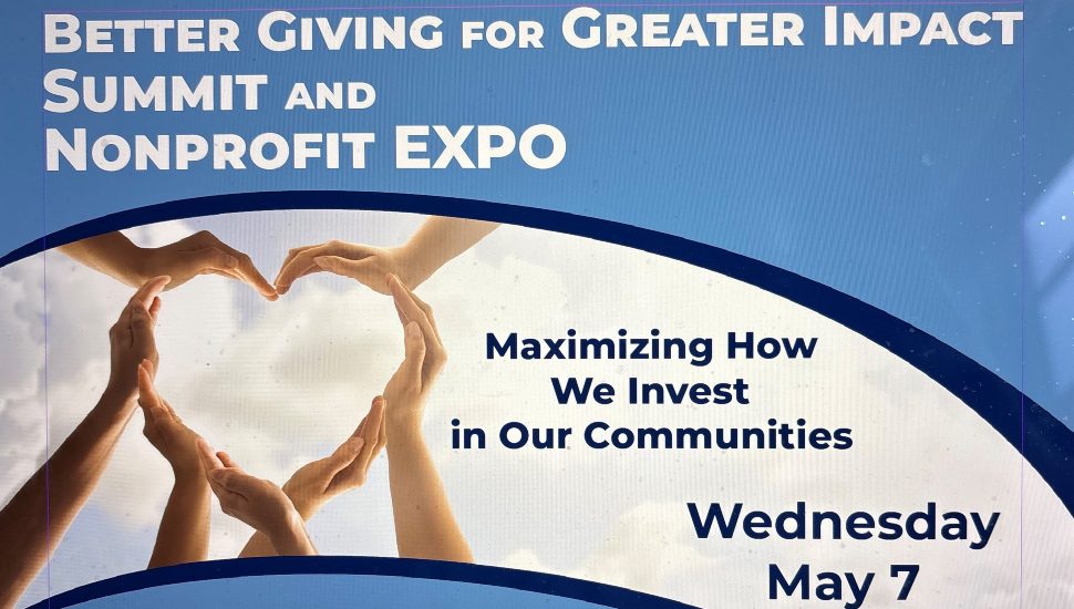Promotional banner for the “Better Giving for Greater Impact Summit and Nonprofit Expo.” The event's theme, “Maximizing How We Invest in Our Communities,” is displayed prominently in the center. The date “Wednesday, May 7” is also included. The top half of the image features a blue background with white and light blue text, and the center shows hands forming a heart shape against a cloudy sky backdrop, symbolizing unity and community support.