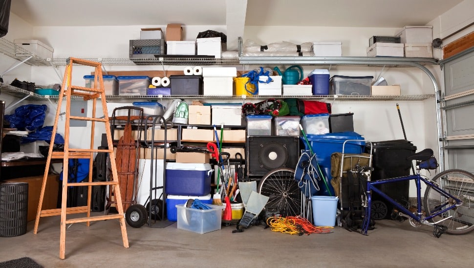 A garage filled with boxes, a ladder, containers and other assorted items.