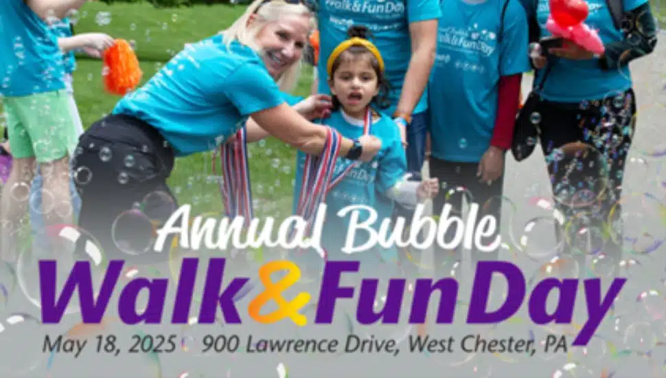 A woman places an award ribbon around a little girl's neck while bubbles float around them.