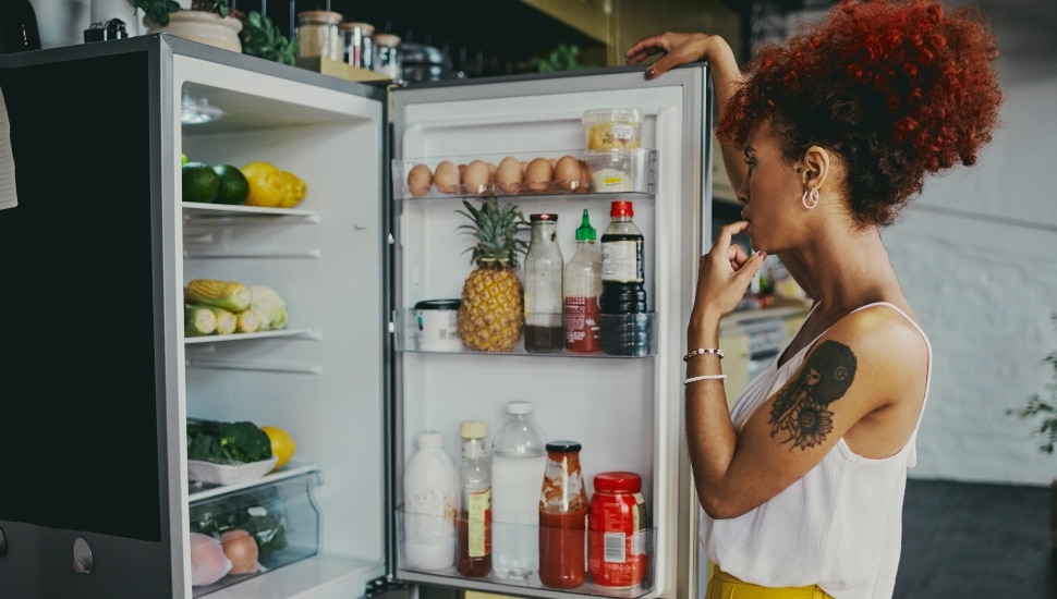 A woman opens a refrigerator door to a refrigerator filled with food.