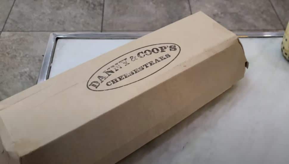 A cardboard box with the Danny and Coops logo containing an authentic South Philly cheesesteak.
