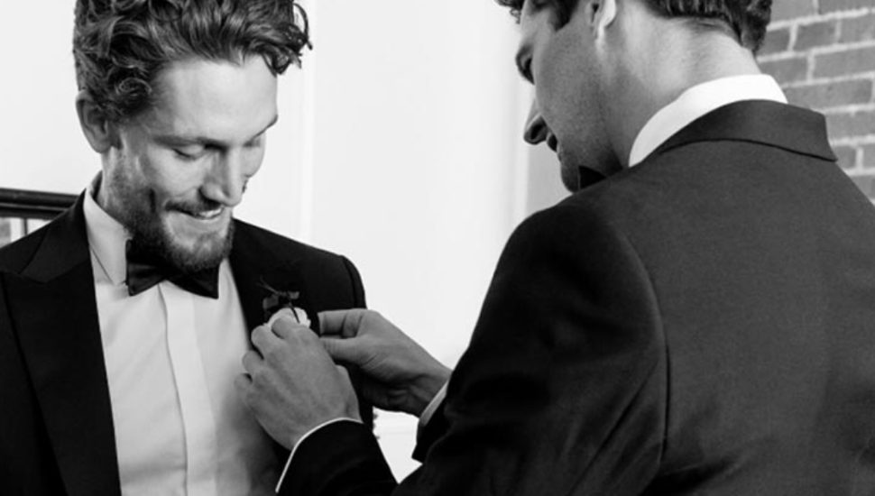 A tailor is helping a groom get fitted for his tuxedo.