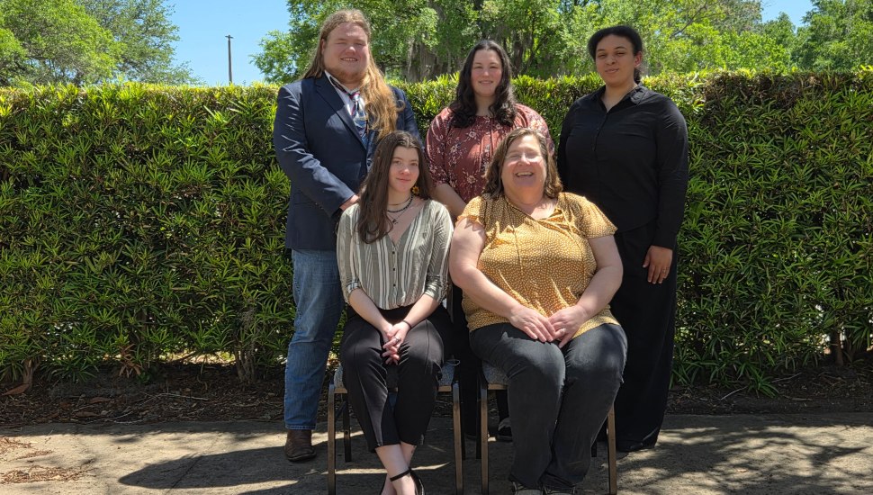College students pose for a group photo in front of bushes.