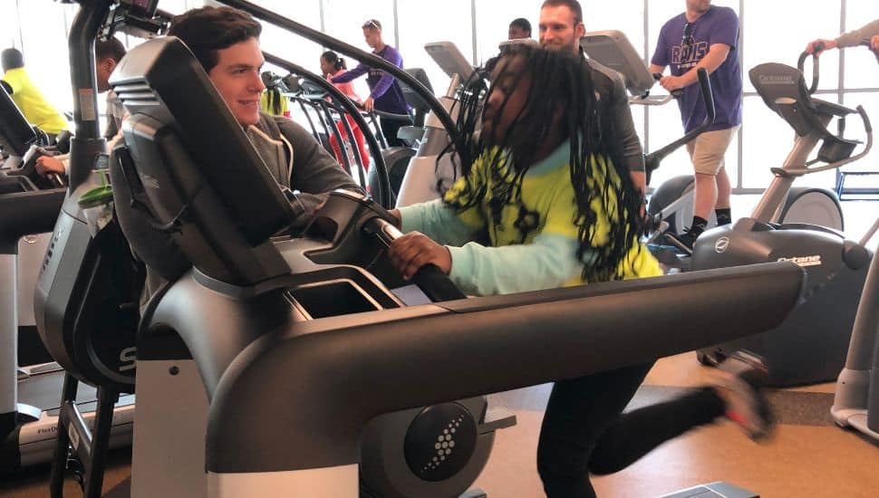 A girl with long hair runs on treadmill at the fitness facility at WCU with a student encouraging her.