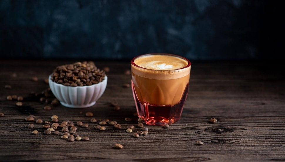 A coffee drink in a glass and a dessert in a cup sit side by side on a table.