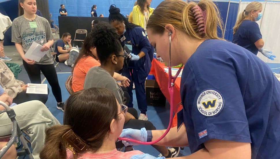 A student nurse in a uniform checks the vital signs of a student posing as a “flood victim” in Widener University's simulated disaster drill.
