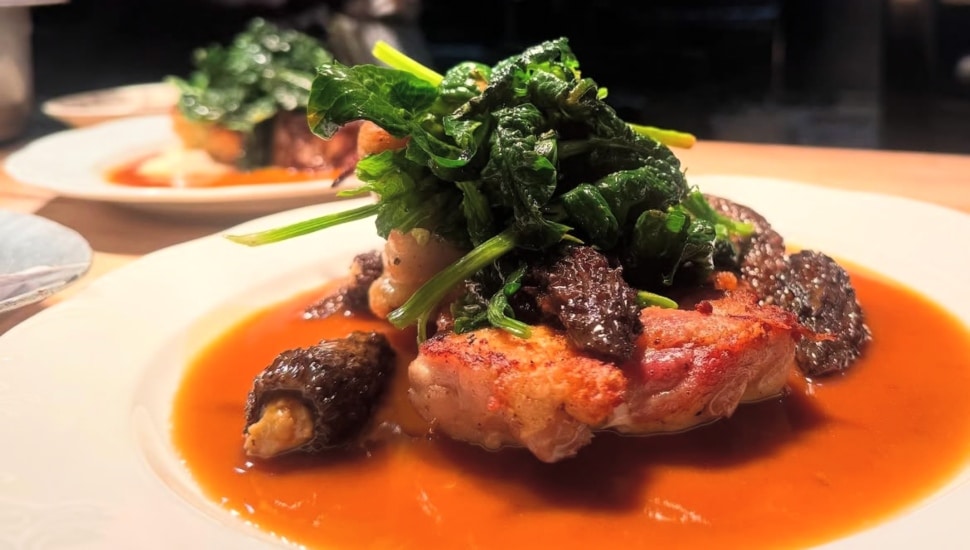 A meat dish with a green vegetable on top, in a plate on a table.