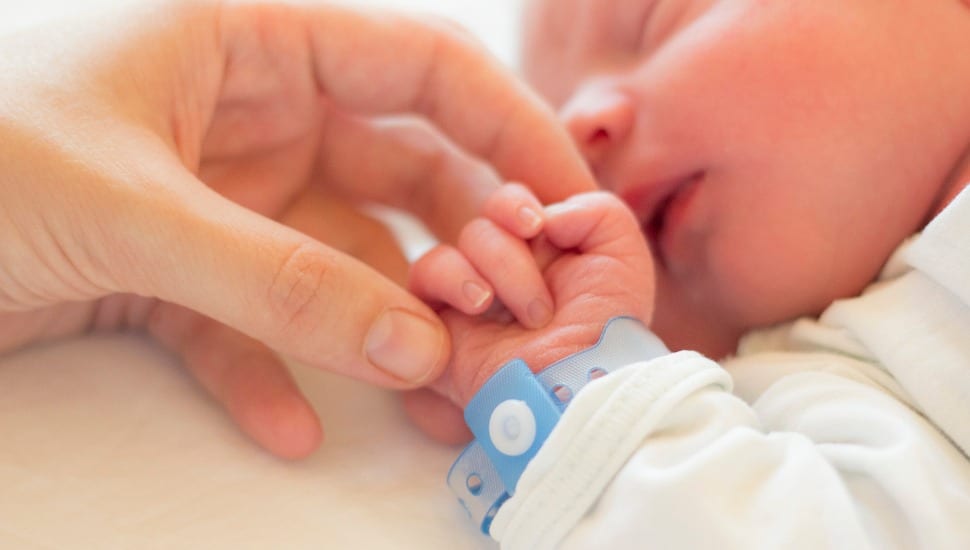 A mother cradles the fingers of a sleeping baby.