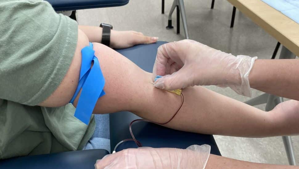A close up photo of a Nurse Aide drawing blood from a right arm. The shirt is rolled up and the arm extended.