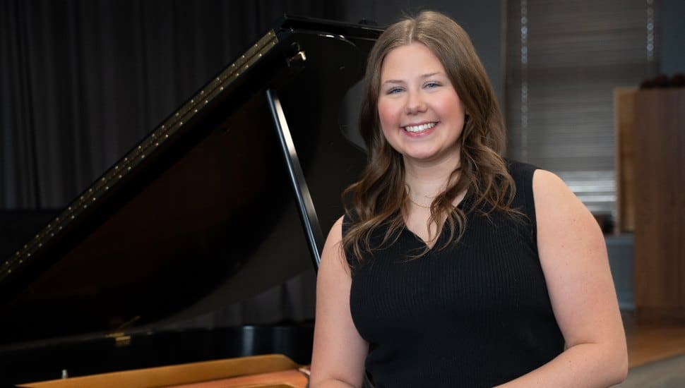 Photo of Olivia Baker with her arm propped on piano.