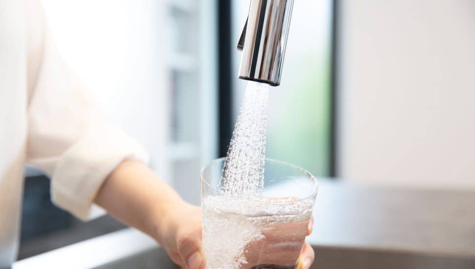 Close up of a hand filling a clear glass with water from the faucet.