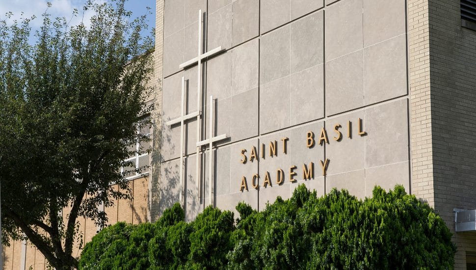 The building and sign for St. Basil Academy, including cross icons, with a tree and shrubbery nearby.