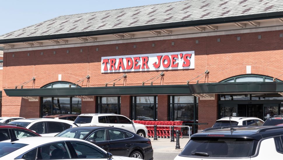 The front of a Trader Joe;s store with sign and a parking lot of cars.